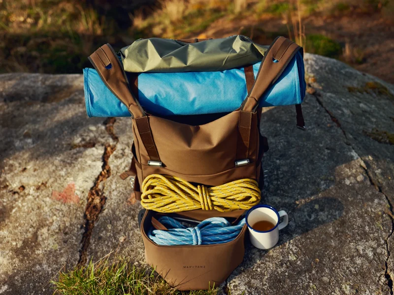Geordnete Ausrüstung auf einem Felsen: Matte, Plane, Seil, Emaillebecher und Rucksack
